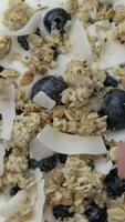 Granola with chia seeds, coconut chips and blue berries in the yogurt turning on the rotating plate. Flat lay video