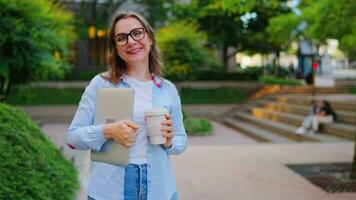 Portrait of woman standing on the street with laptop and coffee in hands video