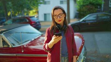 femme est permanent en plein air près le rouge ancien voiture et en utilisant téléphone intelligent video