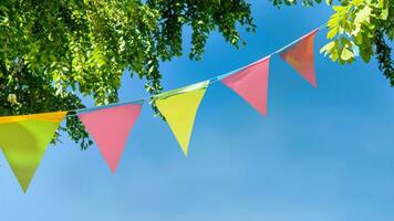 colorful pennant string decoration in green tree foliage on blue sky, summer party background photo