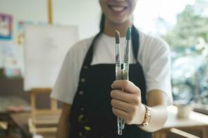 A close-up of the artist hands wearing an apron smeared with paint. Clutching many brushes and paintbrushes. photo