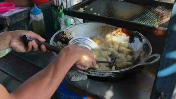 An Indonesian street food vendor serves a customer. A man preparing a dish called 'batagor' to customer on the street video