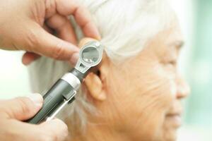 Otolaryngologist or ENT physician doctor examining senior patient ear with otoscope, hearing loss problem. photo