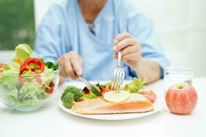 Asian elderly woman patient eating salmon stake and vegetable salad for healthy food in hospital. photo