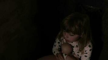Girl of 8 years is hugging the doll sitting in the darkness video