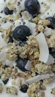 Granola with chia seeds, coconut chips and blue berries in the yogurt turning on the rotating plate. Flat lay video