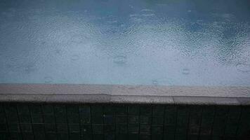Rain drops falling on water surface of blue swimming pool video