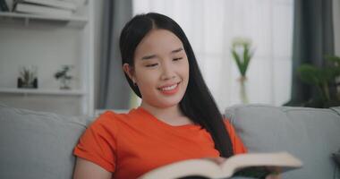 asiático mujer leyendo un libro mientras sentado en el sofá foto