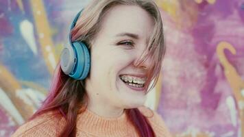 Portrait of a young laughing girl with braces listening to music in headphones in the summer on the street video