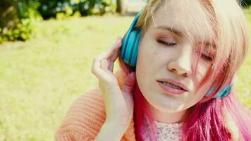 Porträt von ein jung Lachen Mädchen mit Hosenträger Hören zu Musik- im Kopfhörer im das Sommer- auf das Straße video