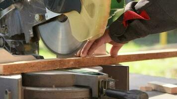 A man uses an electric circular saw to cut wooden bars. Carpenter works on a board outdoors, close-up video