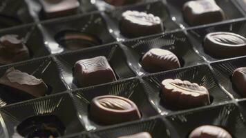 Chocolate candies of various shapes lie in box. Selective focus, slow motion. video