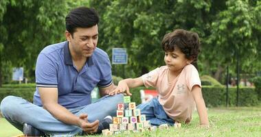 Video of little child boy having fun building construction tower from blocks with father in park