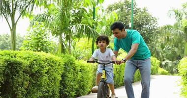 Video of father teaching son to ride bicycle in summer park.