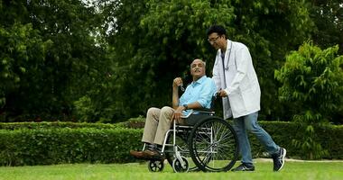 Video of elderly man on wheelchair with caregiver doctor walking in park