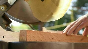 A man uses an electric circular saw to cut wooden bars. Carpenter works on a board outdoors, close-up video