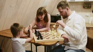 Lycklig familj mor, pappa och deras son spelar schack i de rum video