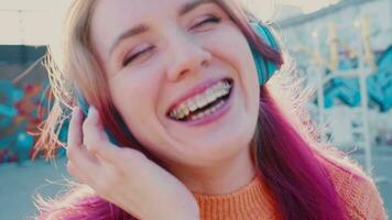 Portrait of a young laughing girl with braces listening to music in headphones in the summer on the street video