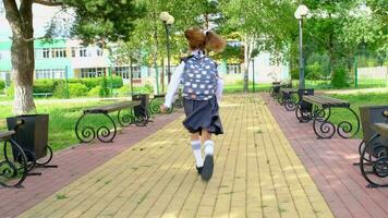 Cheerful funny girl with toothless smile in school uniform with white bows running in school yard. Back to school, September 1. Happy pupil with backpack. Primary education, elementary class. motion video