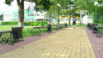 vrolijk grappig meisje met tandeloos glimlach in school- uniform met wit bogen rennen in school- tuin. terug naar school, september 1. gelukkig leerling met rugzak. primair opleiding, elementair klas. beweging video