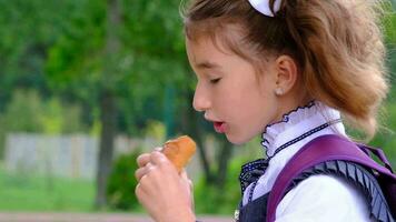Girl with a backpack eating pie near school. A quick snack with a bun, unhealthy food, lunch from school. Back to school. Education, primary school classes, September 1 video