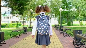 alegre engraçado menina com desdentado sorrir dentro escola uniforme com branco arcos corrida dentro escola quintal. costas para escola, setembro 1. feliz aluno com mochila. primário Educação, elementar aula. movimento video