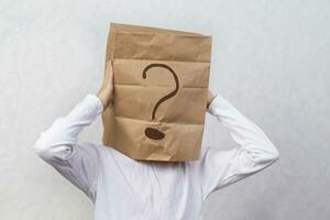 Anonymous man on a gray background with a cardboard box on his head with a drawn question mark. Problems and solutions. Getting answers. photo