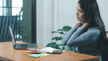 asiatique Jeune femelle avec cou douleur tandis que séance sur bureau travail vente en ligne. video