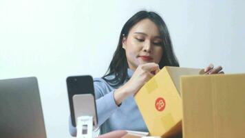 Aziatisch jong zakenvrouw voorbereidingen treffen nieuw bestellingen en controle online aankoop boodschappen doen bestellen naar voorbereidingen treffen pak Product doos Bij huis. video