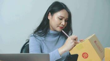 asiático joven mujer de negocios preparando nuevo pedidos y comprobación en línea compra compras orden a preparando paquete producto caja a hogar. video