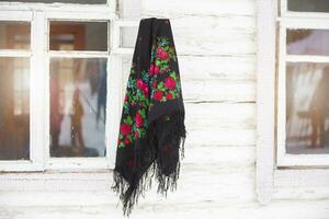 Russian national scarf hangs on the window of a wooden house.. photo