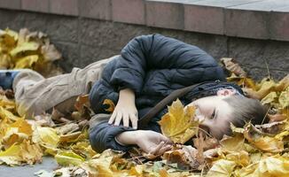 A happy child lies in the autumn leaves in the city. Warm autumn. photo