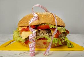 Hamburger wrapped in a measuring tape on a gray background. Weight loss concept. photo