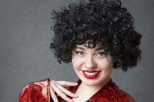 Excited woman in an afro wig on a gray background. Disco girl. photo