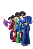 A group of girls in colorful flared suits and afro wigs pose against a white background. Disco style from the eighties or seventies. photo