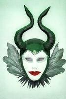 Abstract theatrical mask with horns and feathers on a green background. photo