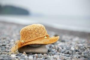 A straw beach hat lies on a pebble by the sea. photo