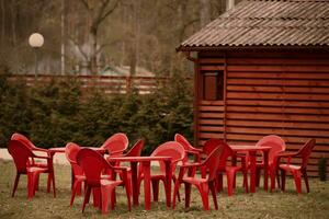 Part of a wooden building and a row of empty red chairs and tables. photo