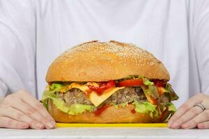 Big burger on the table against the background of female hands. photo