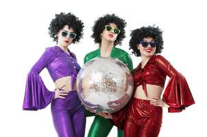 A group of girls dressed in a disco style in shiny multi-colored costumes are holding a disco ball. photo