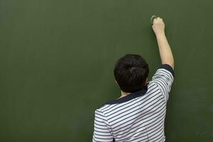 An elderly woman teacher writes with chalk on a blackboard.Back view. photo