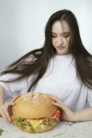 un mujer es participación un grande parilla hamburguesa emparedado en el antecedentes. rápido comida concepto. el niña tiene un enorme hamburguesa. foto