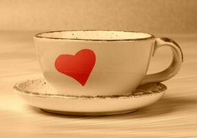 Ceramic cup with painted red heart in beige toning. Morning coffee or tea with love. photo