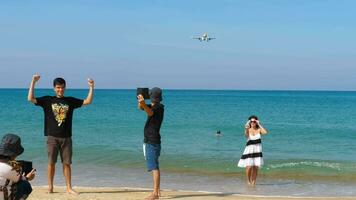 PHUKET, THAILAND JANUARY 23, 2023 - People and flying aircraft. Tropical blue sea. Luxury holiday resort. Island Phuket in Thailand. Impressive paradise. Hot beach Mai Khao. Amazing landscape unique video