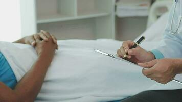 Senior doctor and young male patient who lie on the bed while checking pulse, consult and explain with nurse taking note and supporting in hospital wards. video