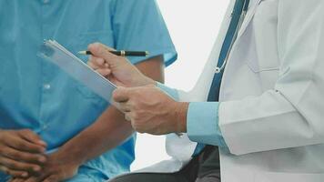 Senior doctor and young male patient who lie on the bed while checking pulse, consult and explain with nurse taking note and supporting in hospital wards. video