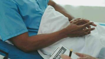 Senior doctor and young male patient who lie on the bed while checking pulse, consult and explain with nurse taking note and supporting in hospital wards. video