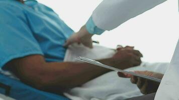 Senior doctor and young male patient who lie on the bed while checking pulse, consult and explain with nurse taking note and supporting in hospital wards. video