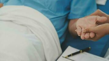 Senior doctor and young male patient who lie on the bed while checking pulse, consult and explain with nurse taking note and supporting in hospital wards. video