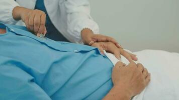 Senior doctor and young male patient who lie on the bed while checking pulse, consult and explain with nurse taking note and supporting in hospital wards. video